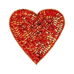 May include: A heart-shaped patch or applique, covered in small, shiny, orange-red sequins. The sequins are densely packed, creating a textured surface. The edges are outlined with a gold-colored trim. The background is plain white.