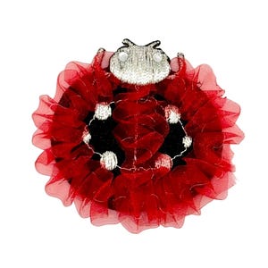 May include: A ladybug-shaped applique featuring a silver embroidered head with two small white circular accents. The body is constructed from layers of ruffled red tulle fabric, accented with silver embroidered circular spots across the surface.