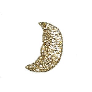 May include: A crescent moon-shaped patch, densely covered in gold sequins, is displayed against a white background. The sequins catch the light, creating a shimmering effect. The edges are outlined with a silver-colored thread.