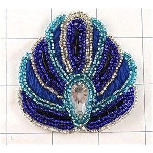 May include: A beaded applique in the shape of a crown, featuring shades of blue, silver, and a central clear gem. The design incorporates various bead sizes and textures, creating a detailed and ornate appearance. The applique is likely for embellishment on clothing or accessories.