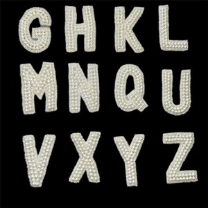 May include: A collection of pearl-covered letters against a black background. The letters include G, H, K, L, M, N, Q, U, V, X, Y, and Z. Each letter is outlined with a pearl-like material, creating a textured, shimmering effect.