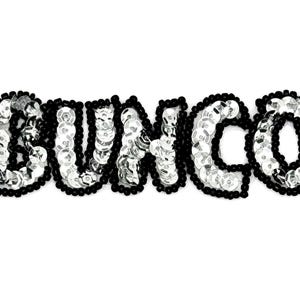 Peut inclure: Un écusson à paillettes épelant le mot "BUNCO" en paillettes argentées. Les lettres sont bordées de perles noires, créant un contraste saisissant sur fond blanc. L'écusson est probablement décoratif.