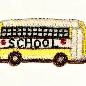 May include: A beaded school bus patch with yellow, white, and brown accents. The bus features black windows, red details, and the word "SCHOOL" in black letters. The patch is embellished with sequins and beads.