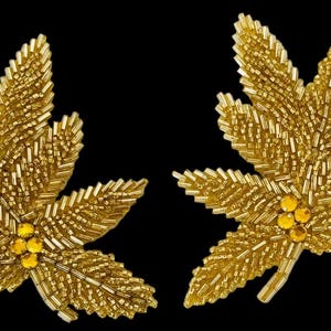 May include: A pair of gold-toned leaf-shaped appliqués crafted from metallic bugle beads and seed beads. Each leaf features a central cluster of three round, amber-colored faceted crystals at the base, creating a textured, shimmering surface.