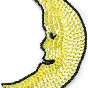 May include: A yellow crescent moon shaped applique made of sequins with black beading around the edges.