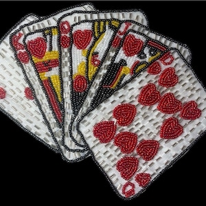 May include: A set of seven playing cards, all hearts, made of white fabric with red and yellow beads. The cards are arranged in a fan shape, with the ace of hearts at the bottom and the queen of hearts at the top.