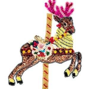 May include: A carousel reindeer patch featuring brown, yellow, and pink sequins. The reindeer has bright pink antlers, a yellow neck, and a floral saddle design. It is attached to a vertical gold pole with red diagonal stripes, all crafted with beads.