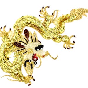 May include: A decorative patch featuring a serpentine dragon crafted with gold sequins and beads. The dragon has a cream-colored head with black and brown beaded accents, a red mouth, and a long, winding body covered in shimmering gold sequins.