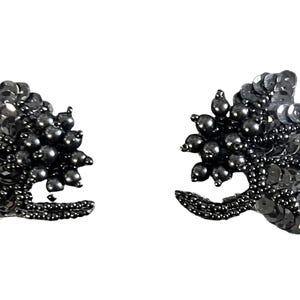 Peut inclure: Une paire d'écussons décoratifs noirs composés d'une dense accumulation de perles sombres et de sequins réfléchissants. Chaque pièce présente une forme de grappe florale ou végétale stylisée avec une tige incurvée, ornée de perles et de sequins.
