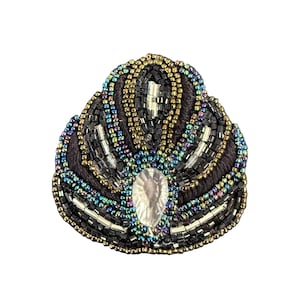 May include: A handcrafted, beaded brooch in a fan shape. The brooch features a central, clear, teardrop-shaped gem, surrounded by intricate beadwork in black, gold, and iridescent colors. The base is a dark brown fabric.