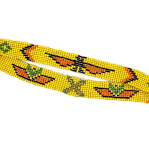 May include: A yellow beaded headband featuring a repeating pattern of orange and black bird-like figures, green geometric shapes, and small orange crescent motifs. The accessory is constructed from small, uniform beads arranged in a flat band.