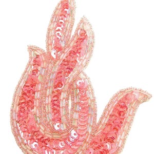 May include: A decorative, pink sequined applique in a stylized flame shape. The applique is filled with pink sequins and outlined with small, clear beads. The design is suitable for embellishing clothing or accessories.