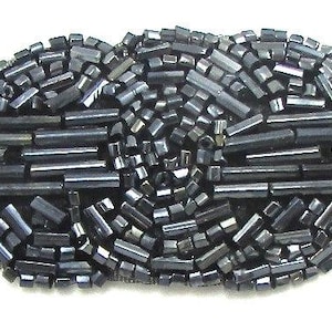 May include: A black beaded embellishment in the shape of a teardrop, with a central design of overlapping circles. The embellishment is made of small, cylindrical beads and is attached to a mesh backing.