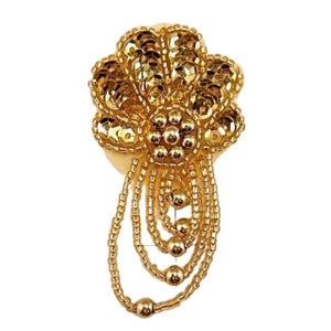 May include: A gold-colored, beaded and sequined floral embellishment. The design features a central flower shape with multiple layers of sequins and beaded strands that hang down. The embellishment is likely for decorative purposes.
