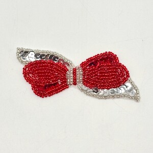 May include: A red and silver beaded bow with a sequined design. The bow is perfect for adding a touch of sparkle to any craft project.
