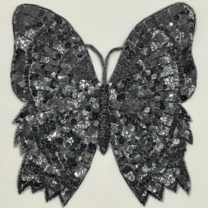 May include: A black sequined butterfly applique. The butterfly is made of black sequins and has a detailed design. It is perfect for adding a touch of sparkle to any project.