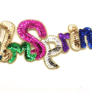 May include: A colorful "Palm Springs" patch made of sequins. The letters are in a variety of colors, including red, pink, green, blue, and gold.