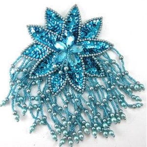 May include: A turquoise sequined flower-shaped brooch with beaded fringe. The brooch features a central cluster of clear beads and a detailed petal design. The fringe consists of strands of small, silver-colored beads.