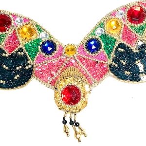 May include: A colourful beaded belly dance belt with a large red jewel in the centre. The belt is decorated with sequins, beads, and jewels in various colours, including pink, green, blue, and gold.