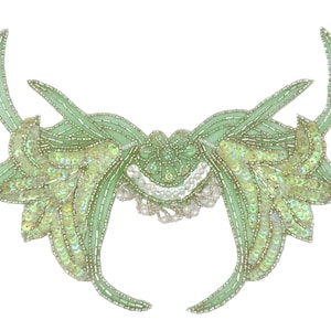 May include: A light green beaded applique with a symmetrical design. The applique features a central floral element, with curved, leaf-like extensions adorned with sequins and beads. The design is embellished with iridescent sequins and small, silver beads.