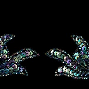 May include: A pair of symmetrical floral-shaped appliqués covered in iridescent, multi-colored sequins. Each piece features a fan-like arrangement of petals in shades of blue, purple, and green, with a dark base and fine beaded edges.