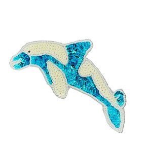 May include: A dolphin-shaped patch featuring a combination of white and bright blue sequins. The design depicts a leaping dolphin with a white upper body and a blue lower body, finished with a white stitched border outlining the entire shape.