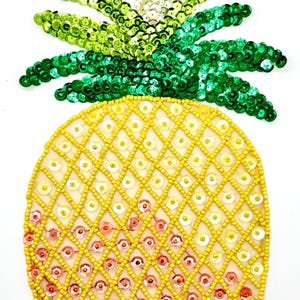 May include: A yellow and green pineapple-shaped patch made of sequins. The pineapple is made of yellow and orange sequins, and the leaves are made of green sequins.