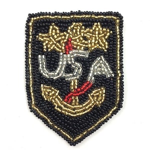 May include: A black beaded patch with a gold border, featuring a gold anchor, two gold stars, and the letters "USA" in silver. Red accents are used throughout the design.