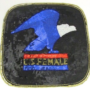 May include: A black square patch with a gold border. The patch features a blue and white sequined eagle with a red and gold sequined banner that reads "U.S. FEMALE".