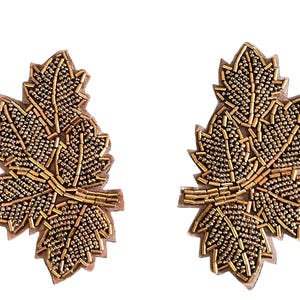 May include: Two leaf-shaped patches featuring intricate gold beadwork and metallic bugle beads. Each patch displays a detailed vein pattern created with elongated beads, set against a tan fabric backing with a die-cut edge following the leaf shape.