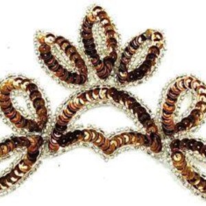 May include: A decorative applique in a crown shape, featuring brown sequins and a silver beaded border. The design includes five petal-like shapes and a curved base, all outlined with silver beads. The applique is set against a white background.