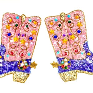 May include: A pair of decorative patches shaped like cowboy boots, featuring pink shafts with gold star and swirl embroidery, purple feet covered in sequins, gold heels, and a multi-colored jeweled spur detail on each boot.