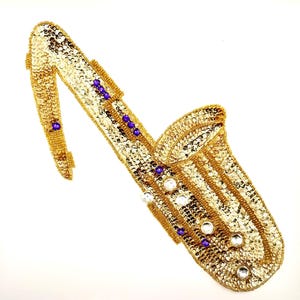 May include: A gold sequined saxophone with purple and white beads. The saxophone is a decorative piece and is not a musical instrument.