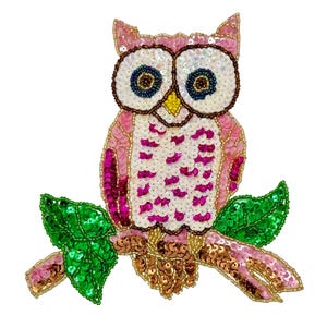 May include: An owl patch crafted with sequins and beads. The owl features a pink and white body with dark eyes, a yellow beak, and sits on a branch with bright green sequined leaves. The branch is detailed with brown and pink sequins.