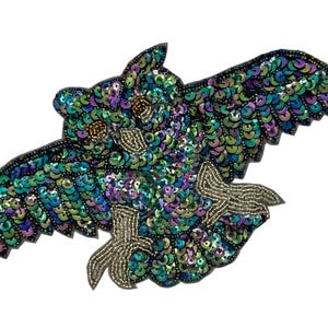May include: An owl-shaped patch featuring iridescent green, blue, and purple sequins covering the wings and body. The owl has gold-toned beaded eyes, a gold-toned beaded beak, and gold-toned beaded talons, all set against a dark backing.