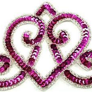 May include: A decorative, heart-shaped applique with a silver beaded border. The applique is filled with pink and magenta sequins, creating a shimmering effect. The design features two intertwined hearts.