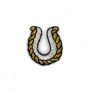 May include: An embroidered patch in the shape of a horseshoe. The design features a metallic gold rope-like border surrounding a white inner section, with thin black outlines separating the colors to create a defined, textured appearance.