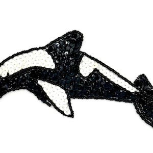 May include: A decorative patch in the shape of an orca whale, crafted with black and white sequins and small black beads. The design features a black body with white patches near the eye and on the side, outlined with black beads throughout.