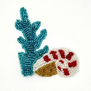 May include: A beaded patch featuring a vertical teal coral branch next to a coiled nautilus shell. The shell is crafted with white beads, accented by red bead patterns and a gold-toned base section, all rendered in a detailed, textured beadwork.