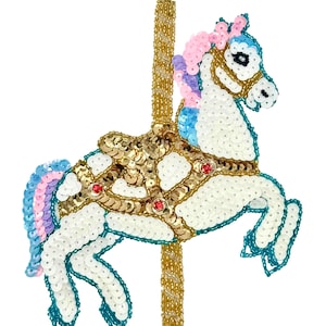 May include: A white carousel horse figurine adorned with sequins and beads. The horse features a gold saddle, a pink, blue, and purple mane and tail, and is accented with red jewels. The pole is gold.