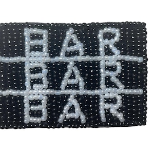 May include: A black and white beaded coaster with the word "BAR" repeated three times.