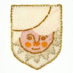 May include: A beaded patch featuring a smiling face with a hat. The face is pink with orange cheeks and a gold outline. The hat and background are white, and the border is gold. The patch is shield-shaped.