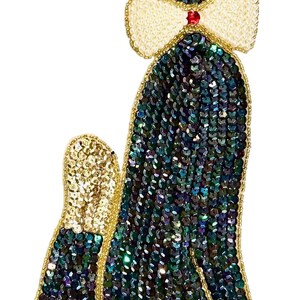 May include: A decorative patch shaped like a sitting cat, covered in iridescent dark blue and green sequins. The cat features gold sequin ears and tail tip, a cream-colored beaded bow tie with a small red center bead, and two white bead eyes.