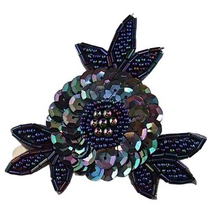 May include: A decorative floral applique featuring dark iridescent sequins and beads. The central flower is composed of layered, shimmering purple and green sequins, surrounded by dark beaded leaves. The entire piece is crafted with intricate needlework.