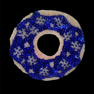 May include: A blue and white donut-shaped sequin applique with a hole in the center. The donut is made of blue sequins with white beads around the edge.