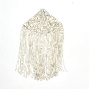 May include: A white beaded accessory with a triangular top and long, dangling beaded fringe. The beads are small and uniformly sized, creating a delicate, textured surface. The piece is likely a vintage or handmade item.