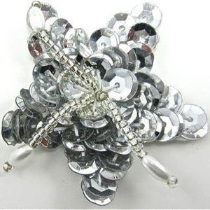May include: A star-shaped brooch crafted from numerous reflective silver sequins layered to create a dimensional effect. The center features a cross-pattern of clear glass beads, with each of the five points tipped with a smooth, white oval pearl bead.