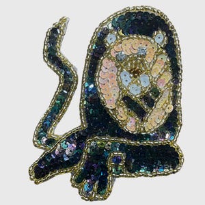 May include: A decorative patch shaped like a monkey, crafted with dark iridescent sequins and light peach-colored sequins for the face. The entire perimeter and facial features are outlined with small gold beads, creating a detailed animal design.