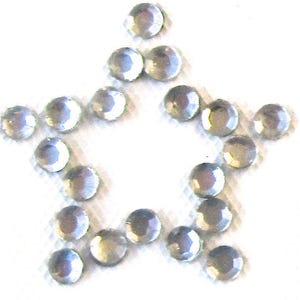May include: A collection of small, clear, circular rhinestones arranged in the shape of a five-pointed star. Each individual stone features a faceted surface that reflects light, creating a bright, shimmering appearance against a plain background.