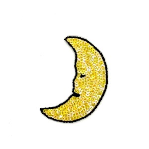 May include: A yellow sequined crescent moon patch with a black border. The moon has a smiling face and is filled with small, shiny sequins. The patch is likely for clothing or accessories.